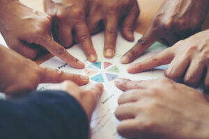Grupo de pessoas apontando para gráfico em papel durante discussão sobre missão e metas de uma empresa.