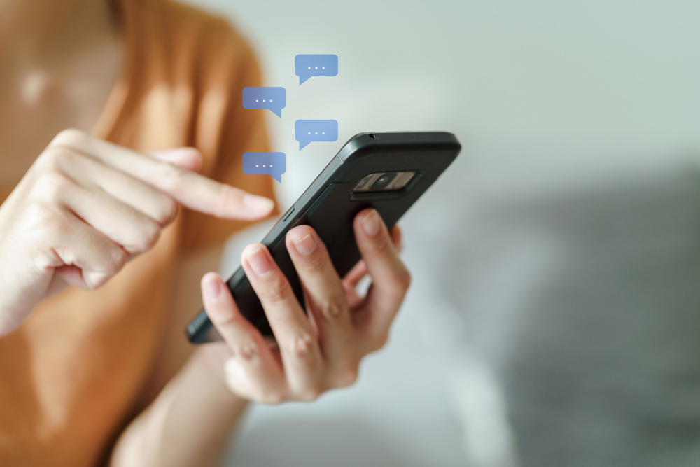 Pessoa digitando no celular com balões de mensagem azuis sobre a tela, simbolizando uma conversa em andamento.
