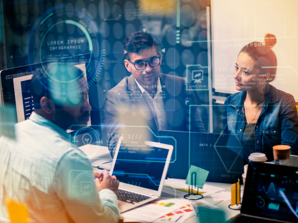 Reunião de profissionais em escritório com computadores, cercados por elementos gráficos digitais que simbolizam inteligência artificial aplicada ao trabalho.