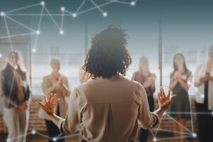 Pessoa liderando uma equipe em reunião, com profissionais ao fundo, representando liderança e engajamento.