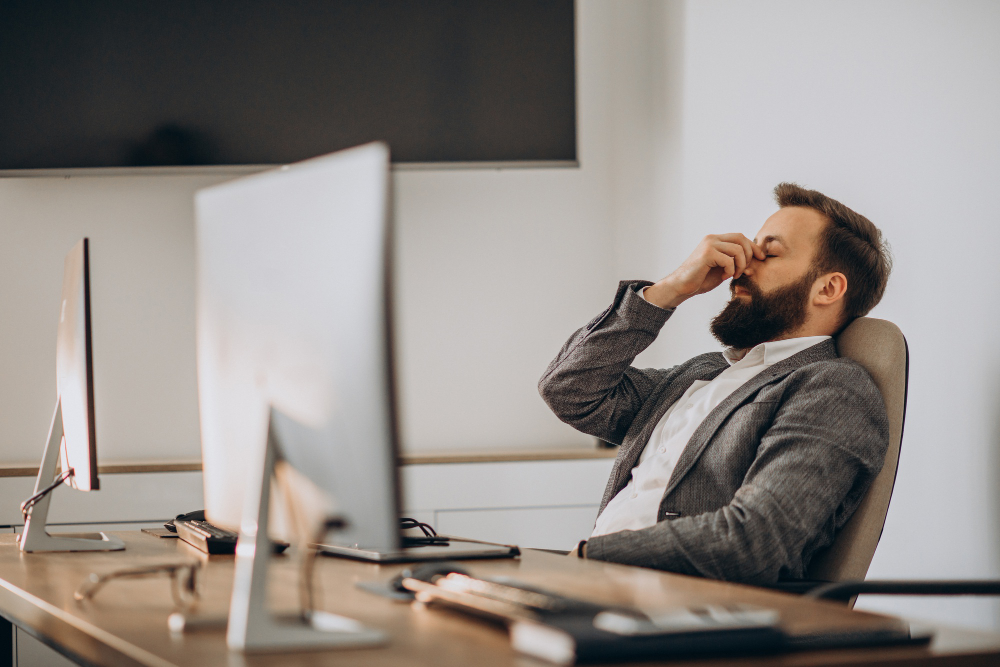 Homem trabalhando em frente ao computador, com expressão de cansaço e estresse, representando os impactos do retrabalho no ambiente corporativo.